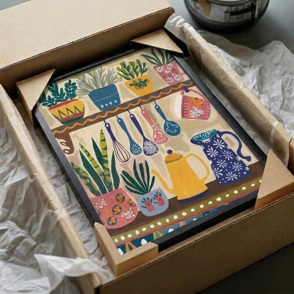May include: Colorful folk art kitchen print in black frame, packed in cardboard shipping box with protective tissue paper. Artwork shows whimsical illustrated kitchen scene with potted plants on shelf, hanging utensils, decorative teapots and mugs in vibrant blues, yellows, pinks and greens. Print features hand-drawn style with floral patterns and botanical elements throughout kitchen items.
