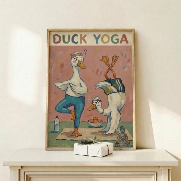 May include: Framed poster showing two cartoon ducks doing yoga poses on a pink and green background, with colorful "DUCK YOGA" text at top. One duck in teal leggings balances on one leg while another duck does a headstand. Small Buddha statue and water bottle visible in scene. Natural wood frame displayed on white wooden shelf with wrapped gift box beside it against cream wall.