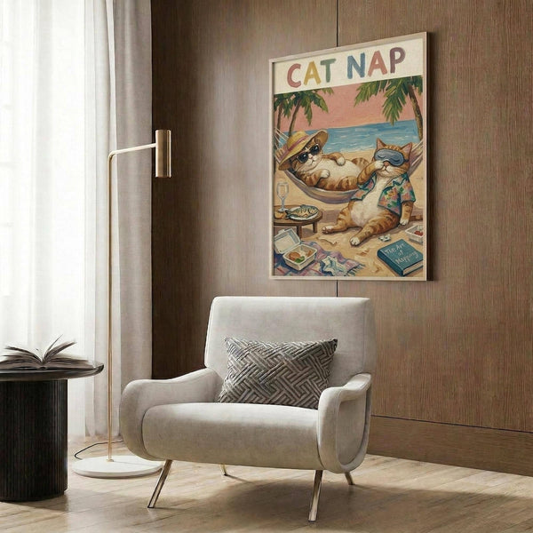 May include: Framed poster print on wood-paneled wall showing cartoon cats relaxing on tropical beach. One orange tabby cat lounging in hammock wearing sunglasses and hat, while gray cat sits nearby in Hawaiian shirt. Beach scene features palm trees, ocean, champagne glass, fish plate, and scattered items on sand. Modern beige armchair with geometric pillow sits below artwork, alongside brass floor lamp and dark side table with open book.