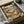 May include: Framed poster print in cardboard shipping box with protective tissue paper. Artwork shows two orange tabby cats relaxing on tropical beach - one lounging in hammock wearing sunglasses and sun hat, another sitting nearby in floral shirt and sunglasses. Scene includes palm trees, ocean, pink sunset sky, beach table with fish dish and wine glass, scattered books and postcards on sand.