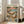 May include: Framed poster print leaning against beige upholstered chair in bright living room with white walls and large windows. The vintage-style illustration shows two orange tabby cats relaxing on a tropical beach - one lounging in a hammock wearing sunglasses and a straw hat, another sitting nearby in a colorful Hawaiian shirt and sunglasses. Scene includes palm trees, ocean backdrop, fish plate, wine glass, and scattered books. Poster has light wood frame and measures approximately 2-3 fe
