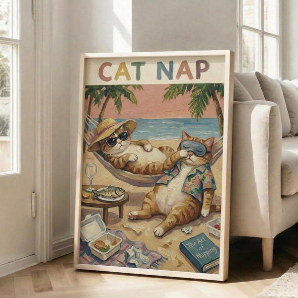 May include: Framed poster print leaning against beige upholstered chair in bright living room with white walls and large windows. The vintage-style illustration shows two orange tabby cats relaxing on a tropical beach - one lounging in a hammock wearing sunglasses and a straw hat, another sitting nearby in a colorful Hawaiian shirt and sunglasses. Scene includes palm trees, ocean backdrop, fish plate, wine glass, and scattered books. Poster has light wood frame and measures approximately 2-3 fe