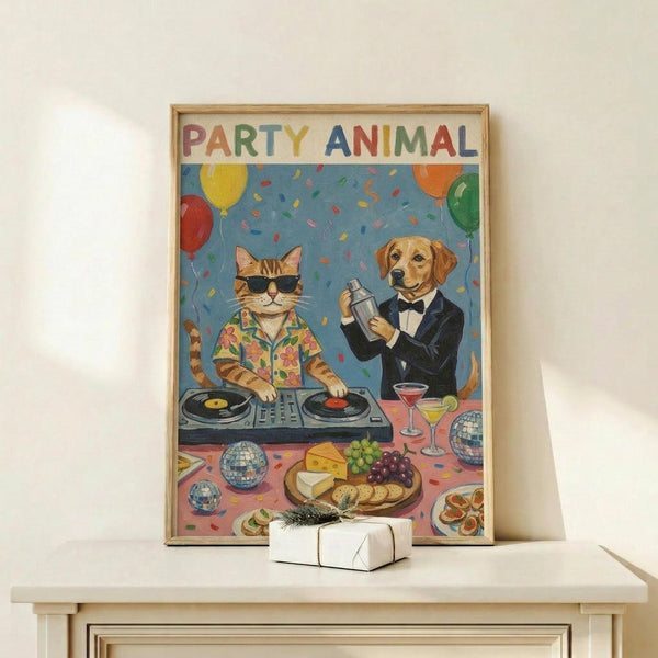 May include: Framed colorful poster showing a cat DJ wearing sunglasses and Hawaiian shirt at turntables, with a golden retriever bartender in tuxedo holding cocktail shaker. Scene includes party balloons, confetti, disco balls, cheese platter, and cocktails on table. Small white gift box with greenery sits on light wood shelf below the artwork against white wall.