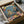 May include: Framed poster artwork being unboxed from cardboard packaging with protective wrapping. The colorful illustration shows a cat wearing sunglasses and tropical shirt operating DJ turntables while a golden retriever in formal tuxedo holds cocktail glasses. Party scene includes balloons, confetti, disco balls, cheese and fruit platter, and wine glasses on pink surface against blue background with "Party Animal" text at top.