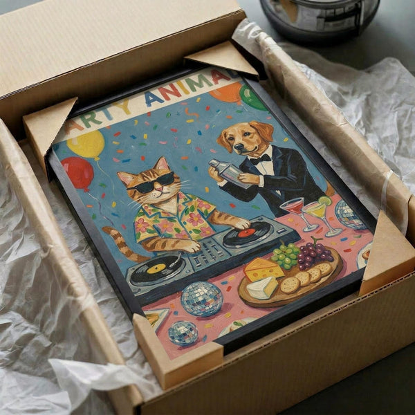 May include: Framed poster artwork being unboxed from cardboard packaging with protective wrapping. The colorful illustration shows a cat wearing sunglasses and tropical shirt operating DJ turntables while a golden retriever in formal tuxedo holds cocktail glasses. Party scene includes balloons, confetti, disco balls, cheese and fruit platter, and wine glasses on pink surface against blue background with "Party Animal" text at top.
