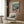 May include: Colorful poster artwork displayed on wood-paneled wall above beige upholstered chair with geometric pillow. Shows cartoon cat DJ at turntables and dog in tuxedo holding cocktail shaker at party with balloons, confetti, and food spread on pink table. Modern living room setting with marble side table, gold floor lamp, and hardwood floors.