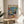 May include: Framed poster print displayed on light wood round side table next to beige upholstered chair. Artwork shows cartoon cat wearing sunglasses and floral shirt DJing alongside golden retriever in black tuxedo holding cocktail shaker. Colorful party scene with balloons, confetti, cheese platter, and cocktails on pink table surface. Blue background with "PARTY ANIMAL" text in rainbow letters across top.