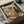 May include: Framed vintage-style poster artwork showing a brown dog wearing sunglasses and artist's smock painting alongside a black cat in beret, surrounded by art supplies, easel, paint palette, wine bottle, and books. The illustration has warm, muted colors and classic artistic studio setting. Frame appears dark colored, nestled in cardboard shipping box with protective wrapping materials visible around edges.