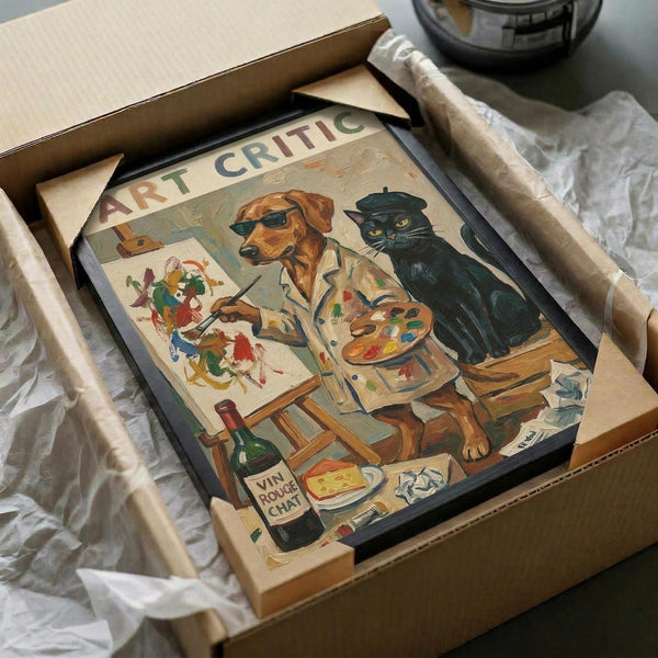 May include: Framed vintage-style poster artwork showing a brown dog wearing sunglasses and artist's smock painting alongside a black cat in beret, surrounded by art supplies, easel, paint palette, wine bottle, and books. The illustration has warm, muted colors and classic artistic studio setting. Frame appears dark colored, nestled in cardboard shipping box with protective wrapping materials visible around edges.