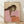 May include: Framed poster print featuring an abstract portrait of a woman with long dark brown hair wearing a pink top, holding a green apple. The artwork uses warm earth tones against a cream background. The print is displayed in a light wood frame, leaning against a white wall on light wooden flooring with soft natural lighting creating gentle shadows.