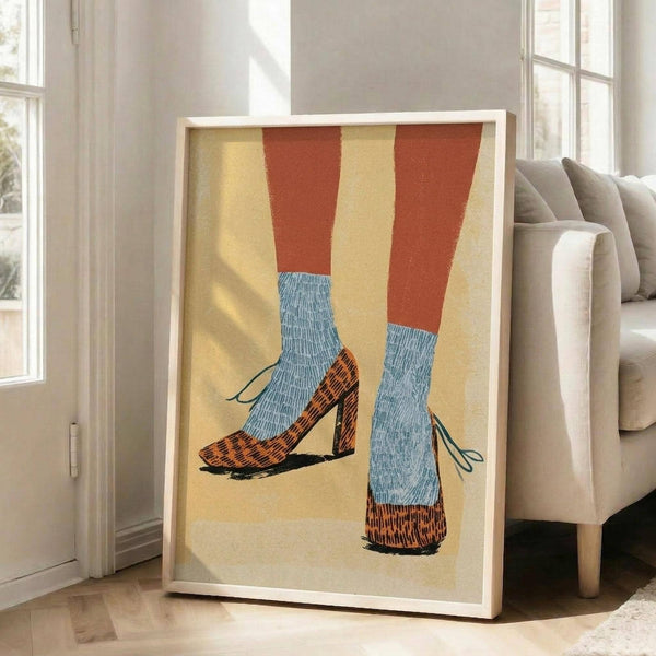 May include: Framed artwork showing legs wearing orange and yellow striped tights with light blue ribbed socks and brown textured heels with ankle ties, displayed on wooden floor against white wall next to beige upholstered chair in bright room with windows