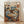 May include: Framed poster print leaning against white wall on light wood floor. Artwork shows two anthropomorphic cats sitting at round cafe table - one tabby in black beret and striped shirt, another orange cat in sunglasses and floral dress. Behind them, coffee machine and cat portraits on wall. Colorful illustrated style with warm browns, blues, and oranges. Natural wood frame.