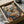May include: Framed poster print in cardboard shipping box with protective wrapping. Artwork shows two anthropomorphic cats in a cozy café setting - one tabby cat in striped shirt and beret, another orange cat in floral dress and sunglasses. They sit at wooden table with coffee, pastries, and newspaper. Background features espresso machine, cat portraits on walls, and "CAT CAFE" text at top. Warm browns, oranges, and blues dominate the vintage-style illustration.