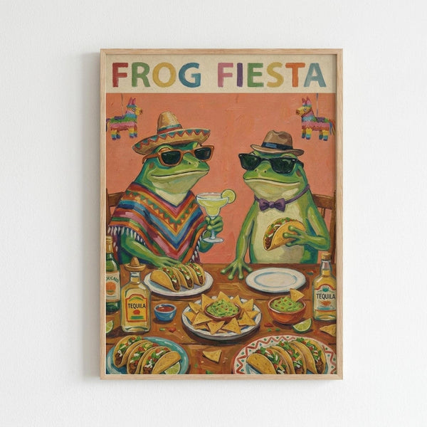 Colorful illustrated poster in light wood frame showing two anthropomorphic frogs wearing sunglasses and Mexican attire at a festive table. Left frog wears a sombrero and striped poncho, holding a margarita. Right frog wears a fedora and bow tie, holding a taco. Table displays Mexican food including tacos, guacamole, chips, and tequila bottles. Orange background features hanging piñatas. Rainbow-colored "FROG FIESTA" text spans the top.