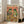 May include: Framed poster artwork leaning against white wall next to beige sofa in bright living room. Print features two cartoon frogs wearing Mexican sombreros and sunglasses at fiesta table with colorful tacos, margaritas, guacamole, tequila bottles, and piñatas. Orange background with multicolored "FROG FIESTA" text at top. White wooden frame, approximately 2-3 feet tall.
