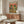 May include: Colorful poster featuring two cartoon frogs wearing sombreros and sunglasses at a Mexican fiesta with tacos, drinks, and party decorations on an orange background. Shown framed in thin wood frame above mid-century walnut credenza in modern living room with white curved chair, glass coffee table, and white table lamp.