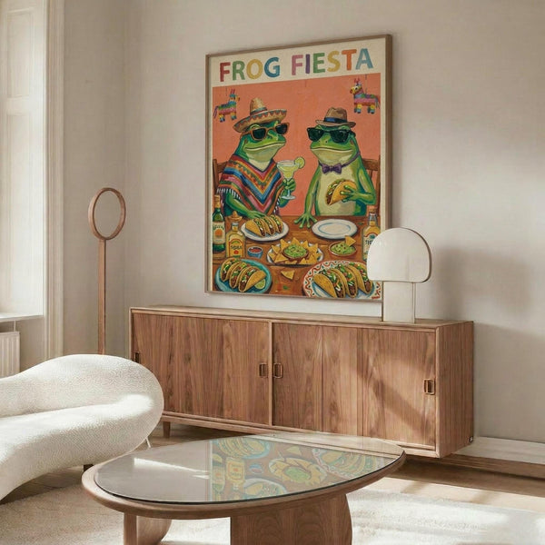 May include: Colorful poster featuring two cartoon frogs wearing sombreros and sunglasses at a Mexican fiesta with tacos, drinks, and party decorations on an orange background. Shown framed in thin wood frame above mid-century walnut credenza in modern living room with white curved chair, glass coffee table, and white table lamp.