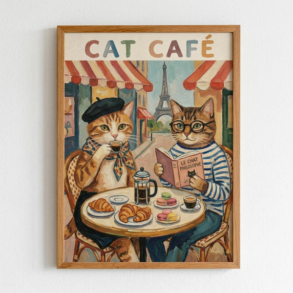 A whimsical illustration showing two anthropomorphic cats sitting at a round cafe table in Paris. One orange tabby cat wears a black beret and patterned scarf while holding a small coffee cup. The other tabby cat wears round glasses and a blue striped shirt while reading a book titled "Le Chat Philosophe." The table holds croissants, macarons, coffee cups, and a French press. Behind them, Parisian storefronts with red and white striped awnings line a street leading to the Eiffel Tower. The artwo