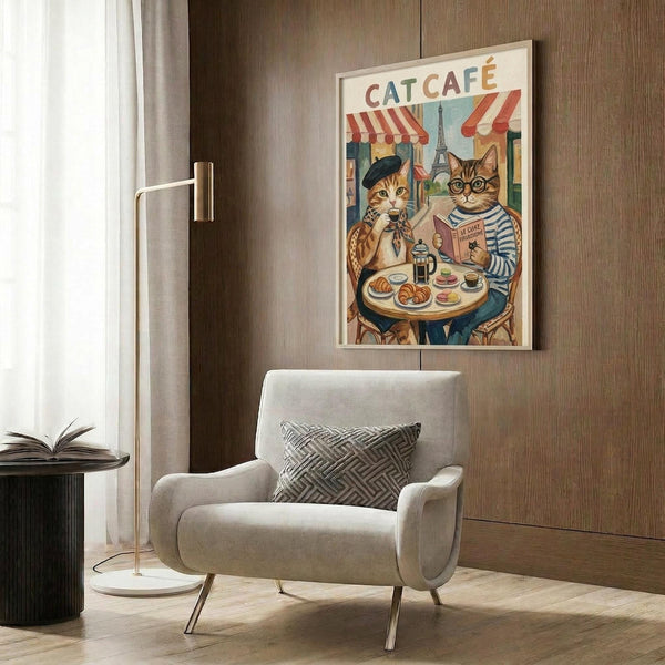 May include: Framed poster artwork showing two anthropomorphic cats at a Parisian cafe table with the Eiffel Tower visible in background. One cat wears a beret and striped shirt while reading, the other wears glasses. The vintage-style illustration features warm colors and cafe awnings. Displayed above a beige armchair with geometric pillow in a modern room with wood paneling, gold floor lamp, and side table with open book.
