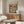 May include: Framed poster showing two cats at a Parisian cafe table with the Eiffel Tower in background. One orange tabby wears a black beret and holds coffee, the other gray tabby in striped shirt reads a French newspaper. Colorful vintage-style artwork with red cafe awnings. Displayed on wooden credenza with white curved chair and glass coffee table in modern living room setting.