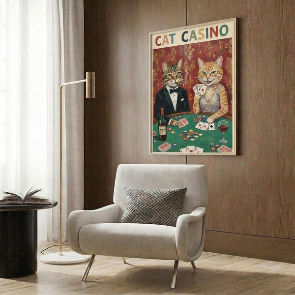 May include: Whimsical poster featuring two cats in formal attire playing poker at a green casino table with cards, chips, and wine. The tabby cat wears a black tuxedo while the orange cat sports an elegant dress. Red fleur-de-lis wallpaper background. Displayed above a cream upholstered chair with geometric pillow in a modern living room with wood paneling, brass floor lamp, and side table.