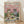 May include: Framed poster print leaning against white wall on light wood floor. Artwork shows two cats wearing sunglasses at picnic on checkered blanket - orange tabby in floral shirt holding wine glass, gray tabby in striped shirt with red bow tie. Pink sky with fluffy clouds above green grass. Picnic spread includes wine bottle, cheese, grapes, fish, and bread. Colorful vintage-style illustration in natural wood frame.