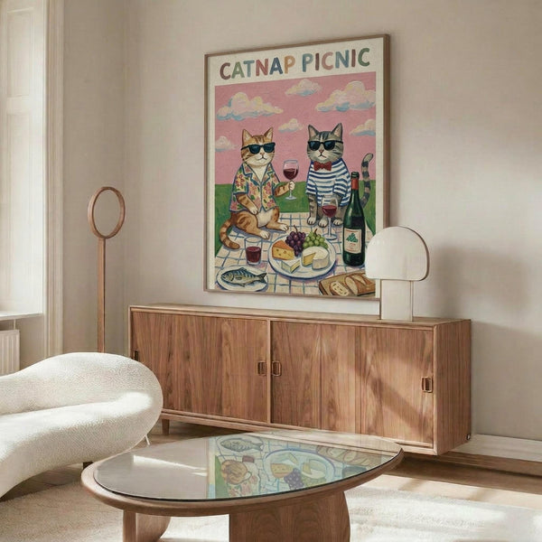 May include: Framed poster showing two cats wearing sunglasses having a picnic with wine, cheese, and grapes under a pink sky, displayed above a mid-century modern walnut credenza in a minimalist living room with white upholstered chair and glass coffee table