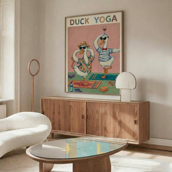 May include: Framed whimsical illustration of two cartoon ducks doing yoga poses on colorful mats, one wearing a floral shirt and sun hat, the other in striped shirt holding a wine glass, displayed above a mid-century modern walnut credenza with white mushroom lamp in a minimalist living room with cream walls, white upholstered chair, and glass-top oval coffee table.