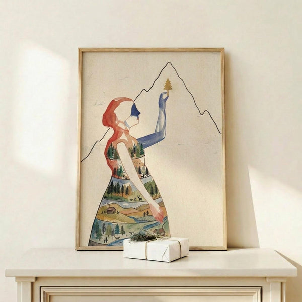 May include: Framed art print on light wooden shelf showing watercolor silhouette of woman with red hair reaching toward mountain peak, her body filled with forest landscape scenes including trees, cabins, and rivers. Small white wrapped gift with evergreen sprig sits beside the natural wood frame against cream wall.