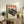 May include: Vintage-style Japanese poster featuring red turntable with vinyl record, Mount Fuji backdrop, and Japanese text, displayed in light wood frame on rustic wooden sideboard next to fern plant, ceramic vase, and books in cozy living room with beige chair and pillows