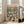 May include: Framed poster leaning against white wall next to beige sofa showing two cartoon ducks in sunglasses on a yacht deck at sunset. One duck wears a straw hat and floral shirt, the other a sailor cap and striped shirt. They're toasting with champagne glasses surrounded by gourmet food including lobster, caviar, cheese and fruit. Orange sunset sky reflects on blue water with boats in background.