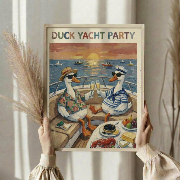 May include: Person holding framed poster showing two cartoon ducks in sunglasses on yacht deck, toasting champagne glasses at sunset. One duck wears Hawaiian shirt and sun hat, other in sailor outfit. Luxury foods like caviar, lobster, cheese spread on boat table. Orange sunset over blue ocean with other boats visible. Light wood frame against neutral background with dried pampas grass visible.