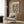 May include: Framed poster hanging on wood-paneled wall above beige upholstered armchair with geometric pillow. Artwork shows two cartoon ducks in sunglasses on yacht deck at sunset - one in floral shirt, one in striped sailor outfit, toasting with champagne glasses. Caviar and appetizers on table. Modern floor lamp and side table with open book visible in styled room setting.