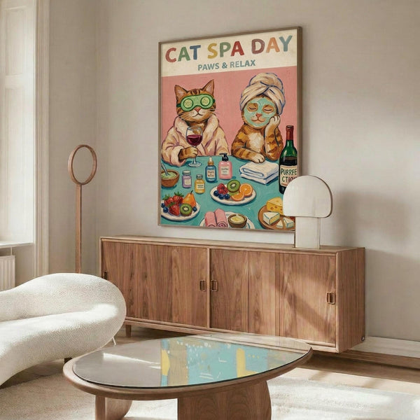 May include: Framed poster print displayed above wooden sideboard in modern living room. Two cats at spa table - orange tabby wearing cucumber eye mask and robe holding wine glass, orange cat with face mask and head wrap. Table has colorful fruits, spa products, wine bottle labeled "PURRFECTION". White curved chair and glass coffee table in foreground. Warm wood tones and neutral walls create cozy interior setting.