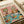 May include: Vintage-style poster print on white paper showing two orange tabby cats enjoying spa treatments. One cat wears cucumber eye mask and holds wine glass, the other has towel headwrap and green face mask. Colorful illustration includes spa bottles, fruit platter, cheese, and book on turquoise table. Warm pink background with "CAT SPA DAY PAWS & RELAX" text at top.