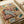 May include: Vintage-style illustrated poster showing two orange cats in a cozy living room scene. One cat wearing striped blue pajamas and sleep mask naps on a brown leather armchair, while another in plaid shirt reads a book nearby. Small fish on a plate sits on wooden floor beside colorful yarn balls and woven rug. Title "CAT NAP" appears in colorful block letters at top. Poster displayed on white surface with rolled paper tube visible.
