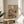 May include: Framed poster with colorful "CAT NAP" text showing two anthropomorphic cats relaxing on a pink armchair - one sleeping in striped pajamas, another reading while wearing sunglasses. Scene includes fish on plate, yarn ball, and cozy living room details. Print displayed on round wooden side table next to beige upholstered chair with plant shadows casting across white walls in bright, naturally lit room.
