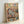 May include: Framed poster print leaning against white wall showing cartoon cats in cozy living room scene. Orange tabby cat in blue striped pajamas and sleep mask naps on brown armchair with "Z" symbols floating above. Second orange cat in green sweater and sunglasses sits nearby reading book. Room details include plate of fish, yarn balls, and warm indoor lighting. Colorful "CAT NAP" text at top in red, green, yellow, pink, blue, and orange letters.
