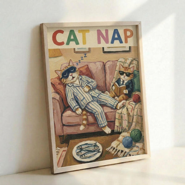May include: Framed poster print leaning against white wall showing cartoon cats in cozy living room scene. Orange tabby cat in blue striped pajamas and sleep mask naps on brown armchair with "Z" symbols floating above. Second orange cat in green sweater and sunglasses sits nearby reading book. Room details include plate of fish, yarn balls, and warm indoor lighting. Colorful "CAT NAP" text at top in red, green, yellow, pink, blue, and orange letters.