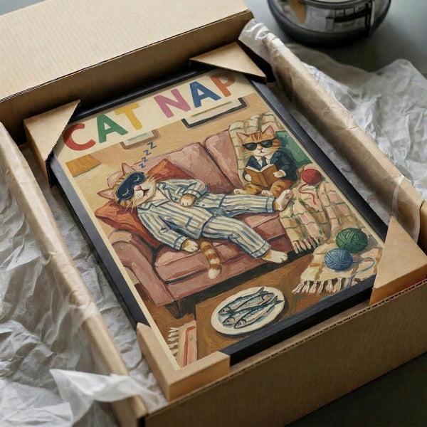 May include: Vintage-style poster print in black frame showing orange tabby cat in blue striped pajamas napping in brown leather armchair. Another cat in suit reads nearby. Colorful "CAT NAP" text at top. Framed artwork packed in cardboard box with protective wrapping on white surface.