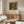 May include: Framed Gustav Klimt reproduction poster featuring colorful wildflower garden with sunflowers in ornate decorative style, displayed above walnut mid-century sideboard in modern living room with white curved chair, glass coffee table, and warm natural lighting on cream walls.