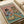 Vintage-style poster print featuring a tabby cat in sunglasses and striped shirt holding a croissant, sitting at a brunch table with a scruffy dog wearing sunglasses and tropical shirt holding wine. Table displays croissants, cheese board, baguette, wine glasses, and dog kibble on teal surface against pink background. Print shown flat on white paper with ribbon nearby.