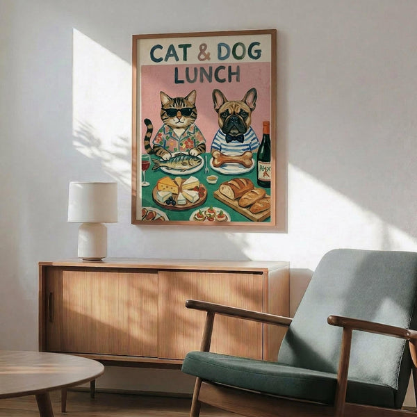 May include: Framed poster displaying illustrated cat wearing sunglasses and Hawaiian shirt sitting beside French bulldog in striped shirt at dining table with fish, bone, cheese, bread and wine. Shown mounted above wood credenza with white lamp in modern living room setting with mint green armchair.