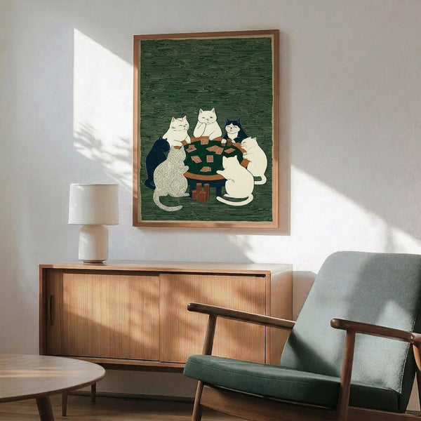 May include: Framed poster print hanging on white wall above wood sideboard with table lamp. Green textured background artwork shows five cats sitting around dark wooden table playing cards. Cats include white, black, and mixed colors in Japanese woodblock print style. Mid-century modern room with teal upholstered chair, round coffee table. Natural sunlight creates shadows on wall.