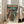 May include: Framed poster with light wood frame leaning against white wall next to beige sectional sofa. Artwork shows anime-style illustration of person in orange spacesuit and helmet standing before large mecha robot in futuristic city setting with neon signs and rain. Features Japanese and Korean text at top. Green and orange color palette with detailed lineart style reminiscent of vintage manga or anime posters.