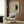 May include: Framed geometric art print featuring a circle split into cream and dark green halves with "HILMA af Klint" text, displayed on wood paneled wall above a beige upholstered armchair with patterned throw pillow, brass floor lamp and dark round side table with open book nearby