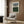 May include: Modern minimalist abstract art print with blue, white, and green horizontal bands and linear details, displayed in light wood frame on warm wood paneled wall above cream upholstered armchair with geometric pillow, brass floor lamp, and dark round side table with open book in contemporary living room setting