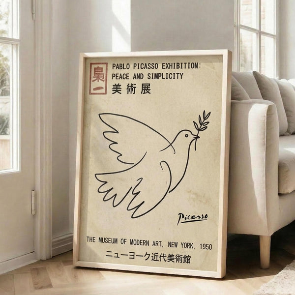 May include: Framed vintage-style exhibition poster featuring Picasso's minimalist line drawing of a dove carrying an olive branch, displayed on light wooden floors against white walls next to a beige upholstered sofa. The cream-colored poster shows black line art with English and Japanese text referencing a 1950 Museum of Modern Art exhibition.