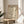 May include: Framed cream-colored poster featuring Picasso's minimalist line drawing of a dove carrying an olive branch, displayed on a round wooden stool next to a beige upholstered chair. Soft natural light creates gentle shadows on white walls. Black text reads "Pablo Picasso Exhibition: Peace and Simplicity" with Japanese characters and "The Museum of Modern Art, New York, 1950" below the dove illustration.