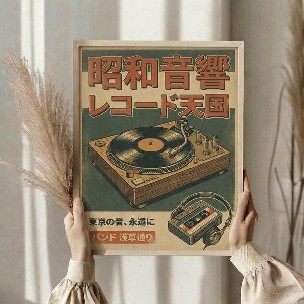 May include: Person holding framed vintage-style poster in natural light. Poster features retro turntable and cassette player illustrations in orange and green color scheme with Japanese text. Light wooden frame complements cream-colored walls and dried wheat stems visible on left side. Soft, minimalist aesthetic with beige tones throughout scene.